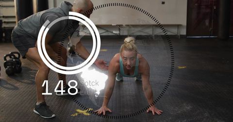 Coach guiding female athlete planking with ar heart rate overlay in gym