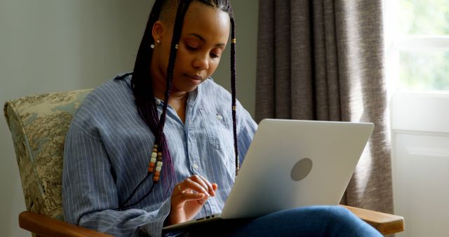 Front view of young black woman working on laptop in a comfortable home. She is sitting on the couch 4k