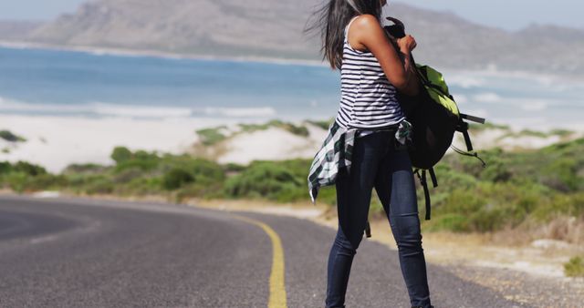African american woman picking up her backpack walking on road. road trip travel and adventure concept