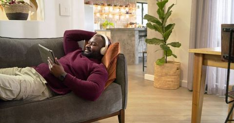 African American man relaxing on sofa with tablet and headphones in cozy living room