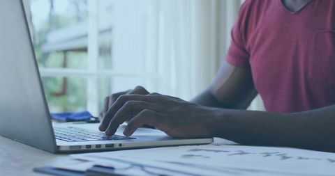 Focused Man in Red T-Shirt Working on Silver Laptop Near Window