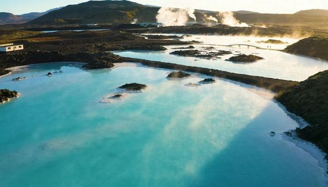 Turquoise geothermal lagoon steaming over black lava fields with footbridge