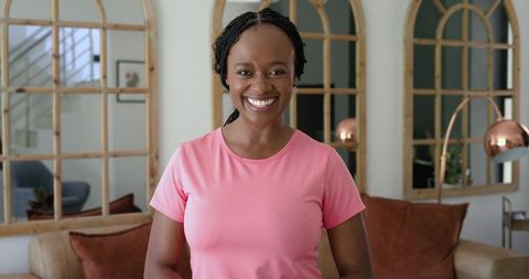 Smiling african woman standing in cozy modern living room wearing pink top