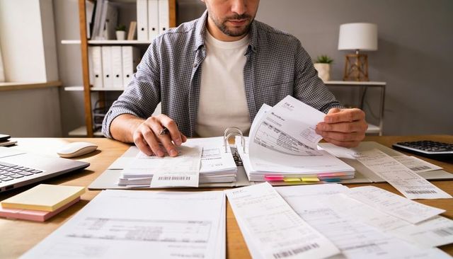 Man sorting invoices and receipts at home office desk reviewing financial documents