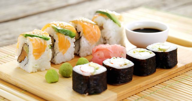 Assorted sushi rolls and nigiri are presented on a bamboo mat, accompanied by soy sauce, wasabi, and pickled ginger. Sushi, a traditional Japanese dish, has gained worldwide popularity for its fresh flavors and artistic presentation.