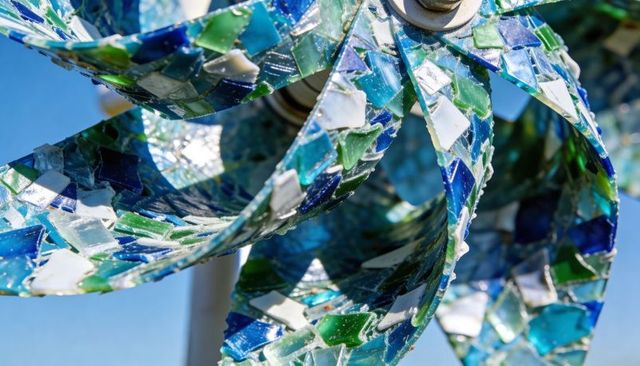 Mosaic glass wind spinner rotating on garden pole, blue-green kinetic outdoor sculpture