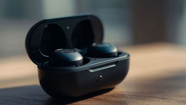 Matte black true wireless earbuds in open charging case on wooden table with led