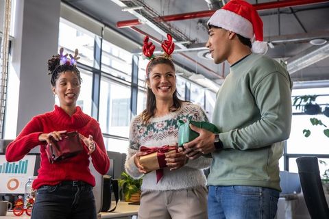 Coworkers exchanging holiday gifts in open-plan office wearing santa hat and antlers