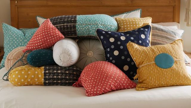 Colorful decorative pillows piling on bed with polka dots, patchwork and textured cushions