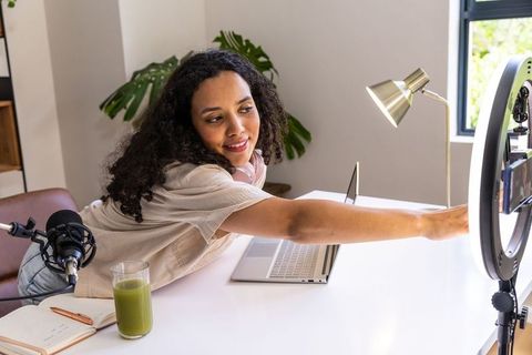 African american woman adjusting ring light and phone creating video content in home studio