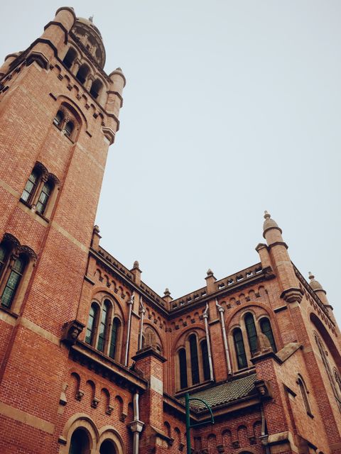 Historic red brick tower displaying Gothic-Renaissance architectural elements. Seen in urban cityscape. Useful for designs emphasizing cultural heritage, architectural marvels, and traditional structures.