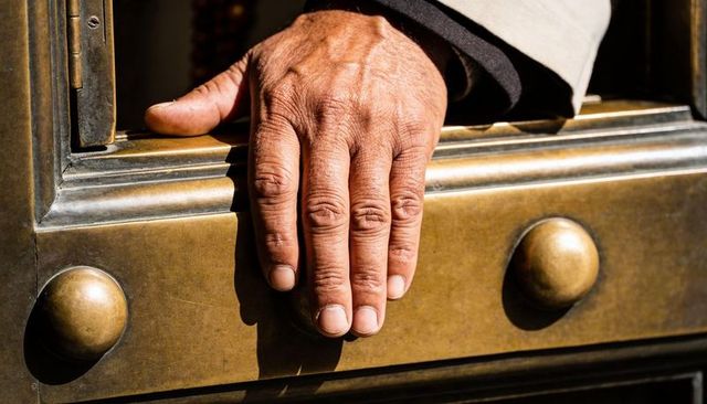 Senior hand resting on polished brass door panel with decorative studs and knob