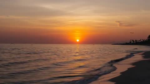 Sunset footage over tropical beach with sun sinking on horizon, waves reflecting golden light