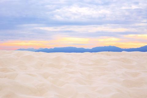 Wandering figure on white sand dunes at pastel sunset with distant mountain silhouette