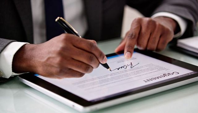 Executive signing digital contract on tablet with pen, touchscreen business agreement