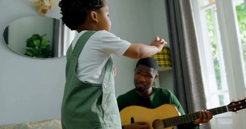 Father Playing Guitar with Toddler Conducting at Home