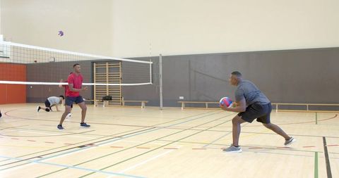 Male teammates practicing volleyball serve and receive drills in indoor sports hall