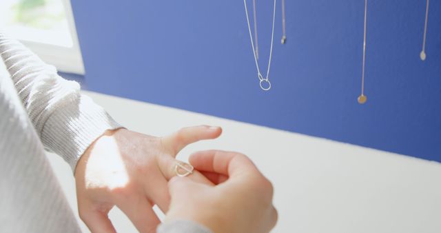 A person is trying on a delicate ring at a jewelry display, with copy space. The setting suggests a casual, intimate shopping experience, in a boutique or at home.
