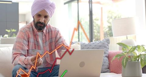 Indian man wearing turban checking laptop with credit card and rising financial charts