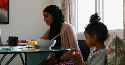 Mother Hijab Working Laptop Beside Daughter Eating Fruit Home