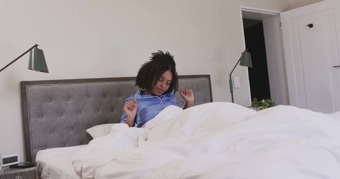 African american woman waking up and checking alarm clock in bright bedroom with duvet