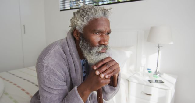 Sick senior african american man sitting on bed at home. Senior lifestyle, domestic life, unaltered.