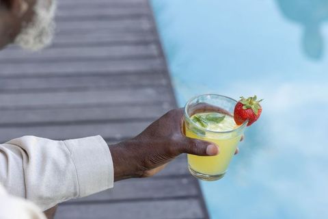 Mature man holding citrus drink by pool on sunlit deck with strawberry garnish