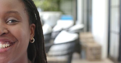 Smiling african woman with locked hair and gold hoop earring on sunlit patio closeup