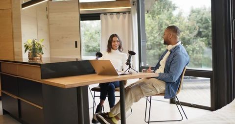 Diverse coworkers recording podcast in modern home studio with laptop and condenser mics