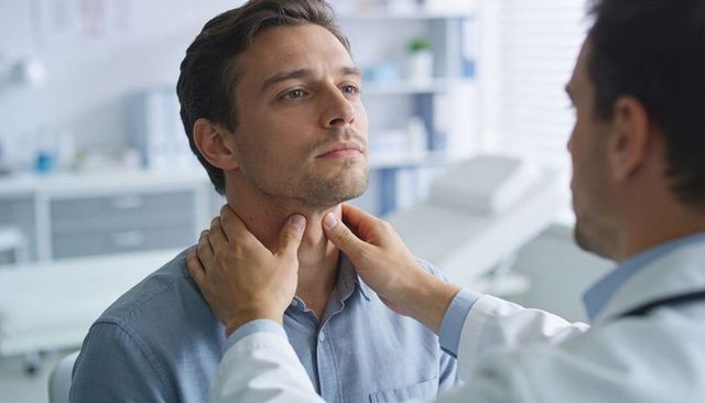 Physician palpating male neck for thyroid examination during clinical checkup in exam room