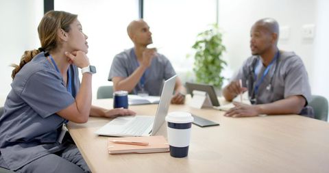 Multiracial healthcare team discussing patient care around conference table with laptop