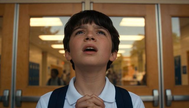 Preteen student looking up with hopeful expression in school hallway near wooden doors
