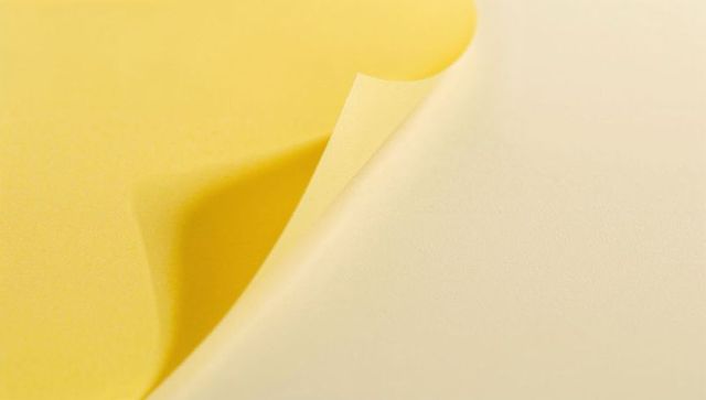 Curling yellow paper revealing cream underside with soft shadow and fine texture