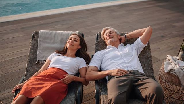 Couple relaxing on poolside loungers at waterfront deck enjoying sunlit leisure and gentle breeze