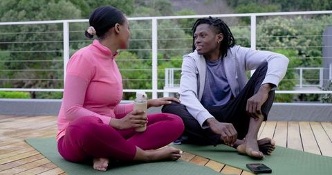 African american couple relaxing on rooftop yoga mats after workout, chatting and hydrating