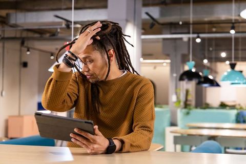 African american man reading tablet and touching forehead in modern coworking lounge