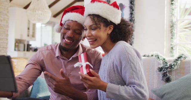 Happy african american couple with santa hats having tablet image call. Spending quality time at christmas together concept.