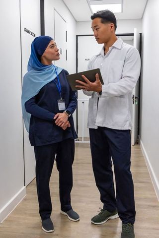 Multicultural healthcare team consulting over tablet in modern clinic corridor
