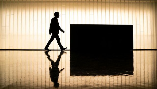 Silhouetted businessman walking past reception desk on glossy lobby floor with reflection