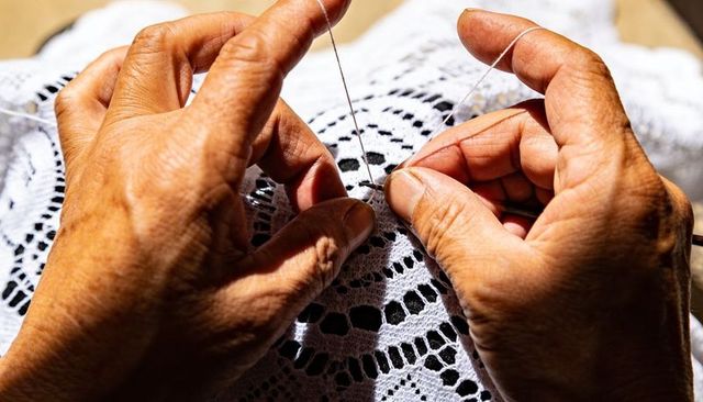 Senior hands crocheting delicate white lace doily in warm sunlight close-up textile craft