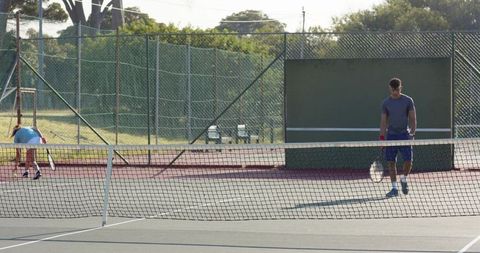 Two tennis players practicing on sunlit outdoor court walking near net and training