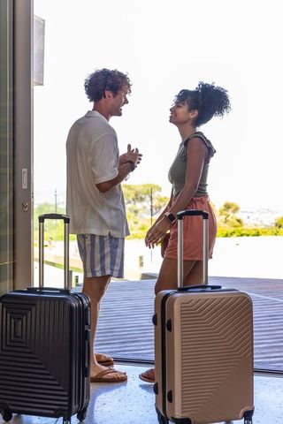 Couple chatting with luggage on sunlit seaside terrace, preparing for summer getaway