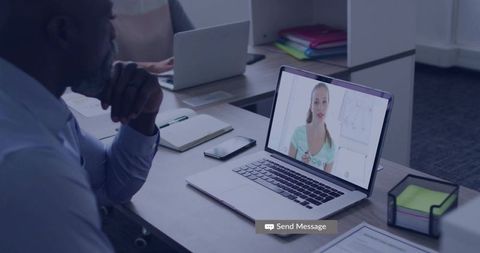 Attentive team member watching laptop video call while colleague types, modern office collaboration