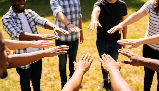 Diverse team forming unity huddle with outstretched hands on sunlit park lawn