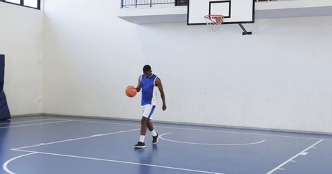 Basketball player dribbling on indoor court in blue uniform