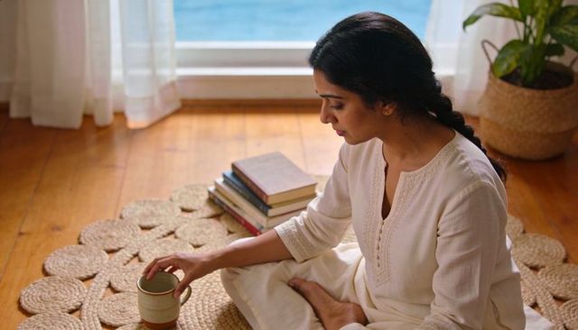 Practicing mindful tea ritual on jute rug by ocean view window, serene morning routine