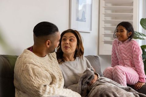 Cozy family bonding on couch sharing playful conversation with daughter in pink pajamas