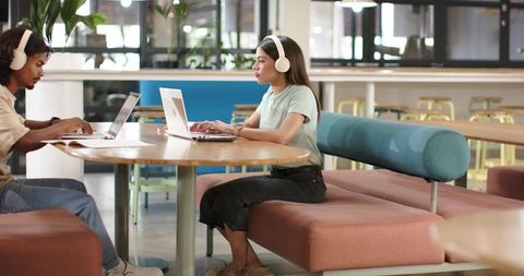 Young woman typing on laptop wearing headphones in bright coworking lounge
