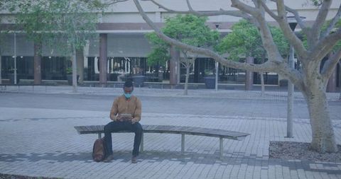 Man in Mask Using Tablet on Urban Bench in Tranquil Setting
