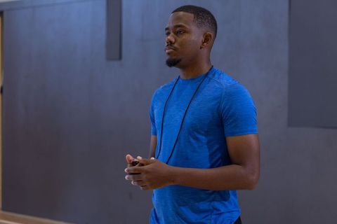 African american fitness coach standing in gym holding stopwatch, blue shirt, focused
